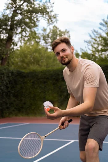 A smiley man playing badminton side view